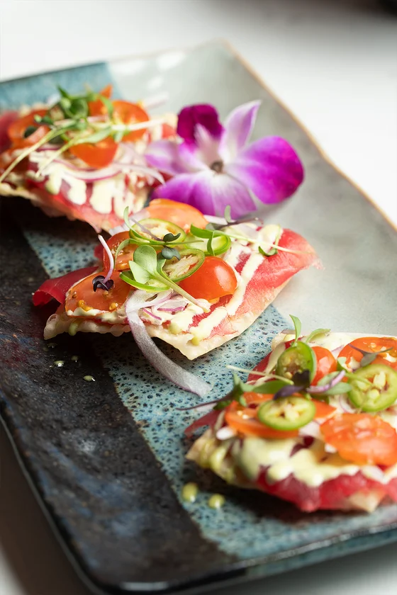 Tuna tostada topped with serrano pepper, cherry tomato, and micro greens.