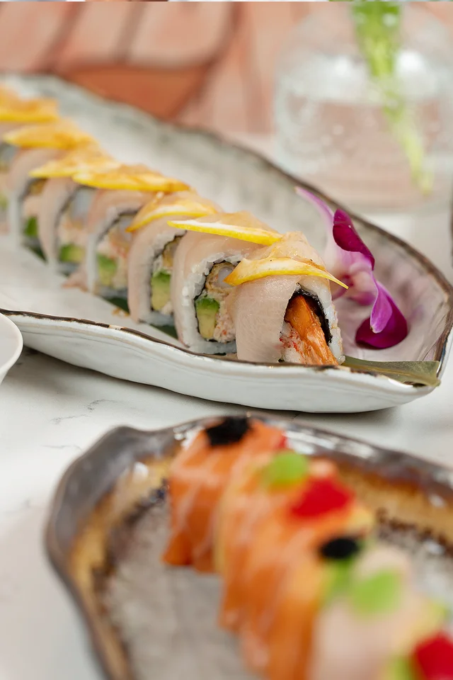 A signature roll topped with seared fish and lemon, garnished with an orchid.